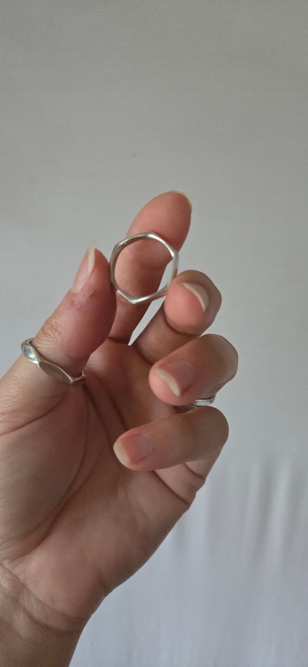 hand holding a silver 6 sided ring, showing the side view, against a white backdrop
