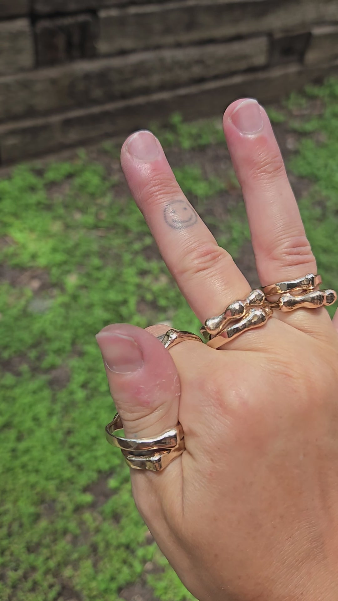 shows a hand, outdoors in bright sunlight, wearing many bronze rings in 2 styles, showcasing how the "orbit ring" spins around the finger.
