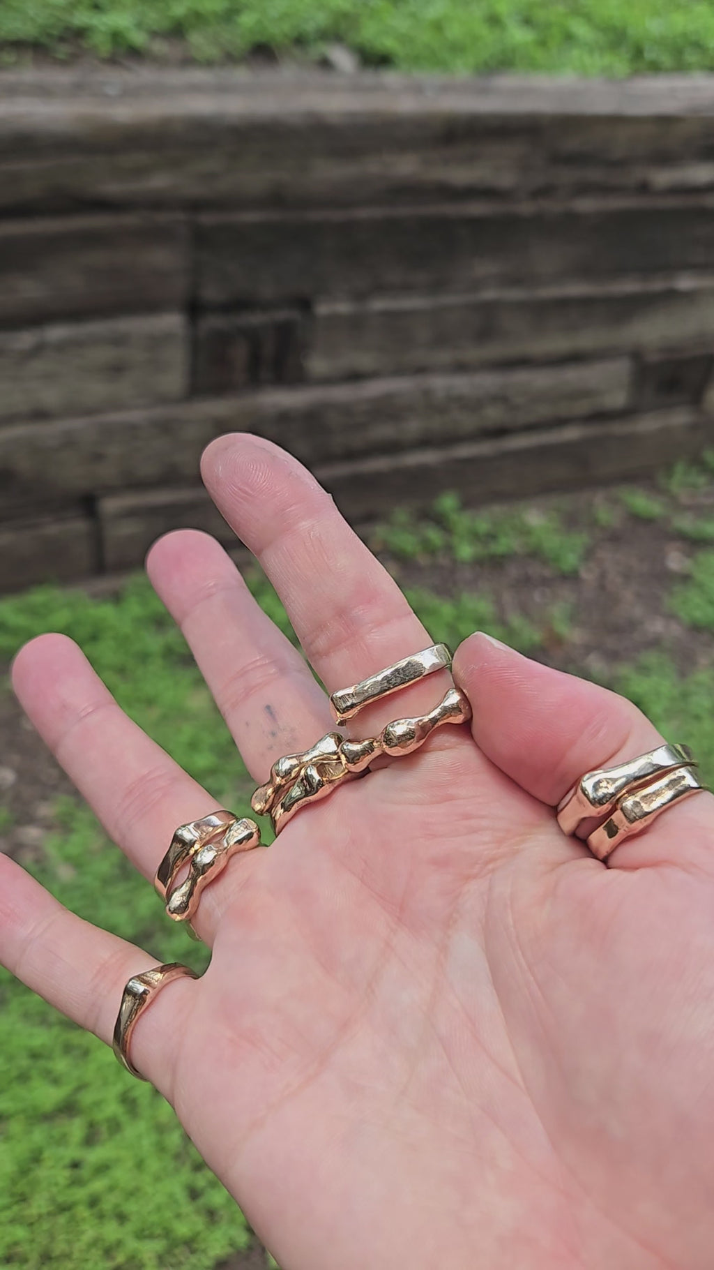 shows a hand in the outdoors in bright sunlight, wearing many bronze gold rings in bright sunlight. the wearer is spinning the "aura ring" around their finger