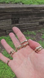 shows a hand in the outdoors in bright sunlight, wearing many bronze gold rings in bright sunlight. the wearer is spinning the "aura ring" around their finger