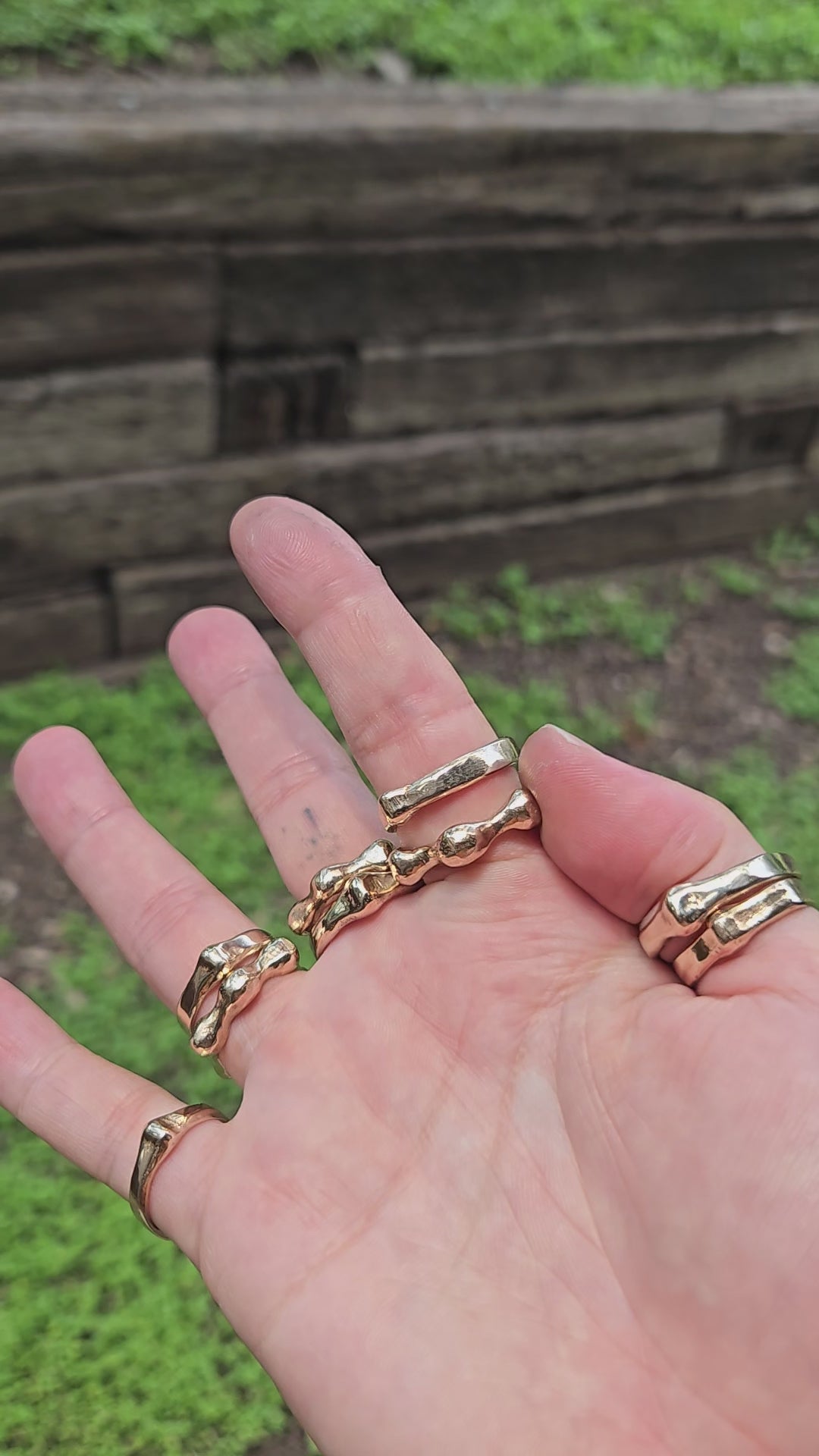 shows a hand in the outdoors in bright sunlight, wearing many bronze gold rings in bright sunlight. the wearer is spinning the "aura ring" around their finger
