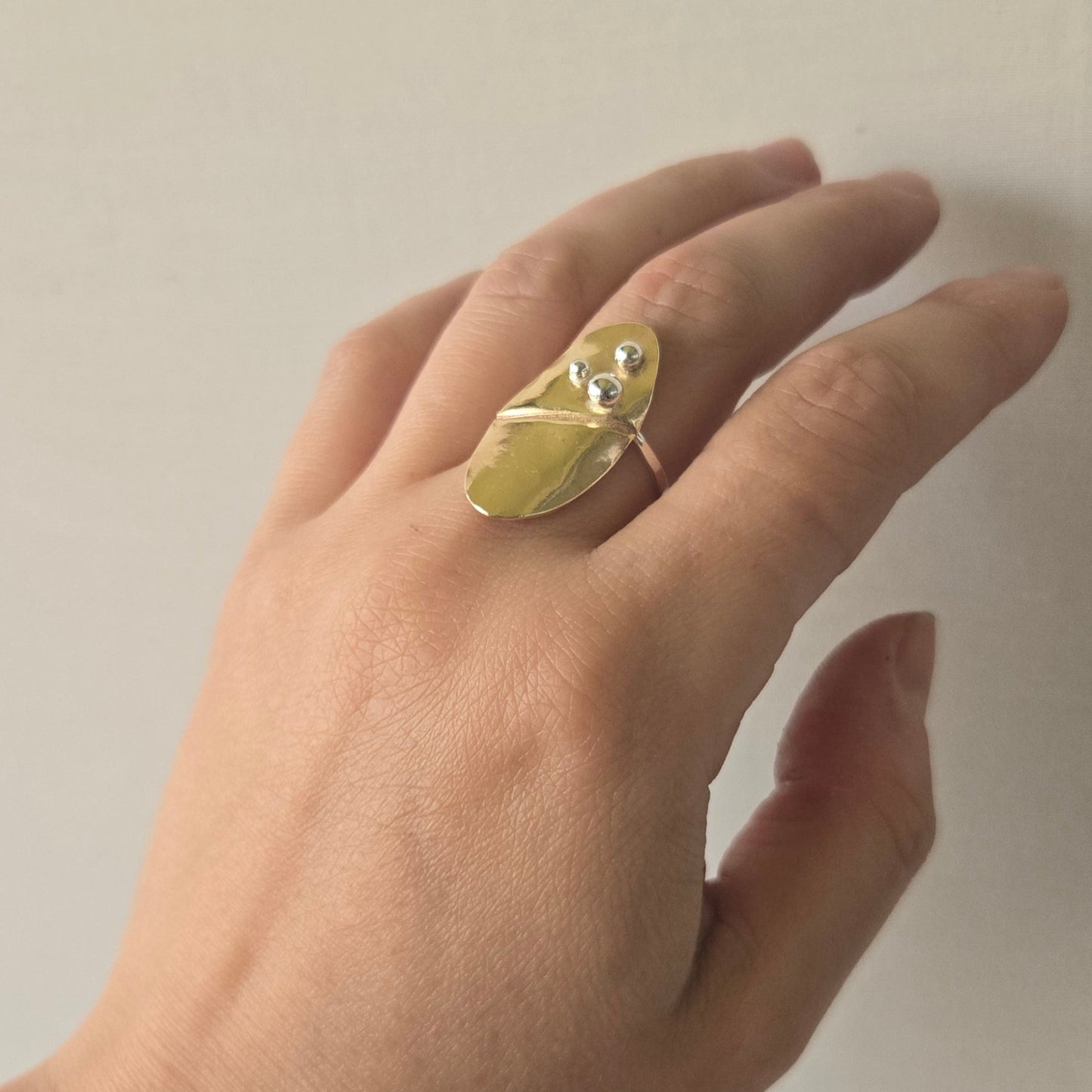 Hand wearing a brass and silver ring on a plain background for slowforge.co