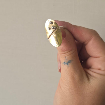 Hand holding a brass oval-shaped Terra Ring against a neutral background for slow forge co